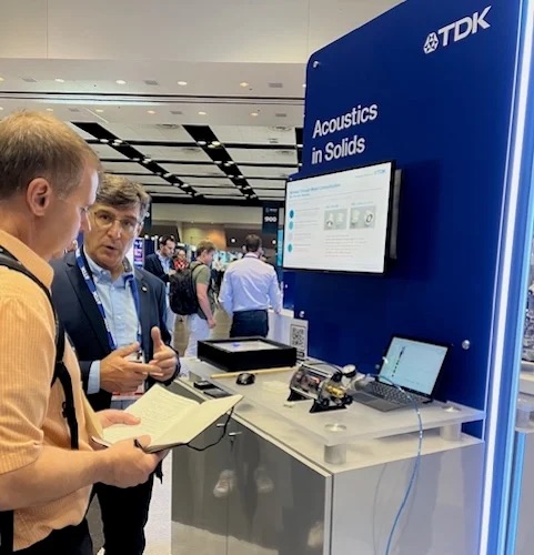At TDK’s Sensors Converge 2024 booth, a representative demonstrates to Dale how they use acoustic waves to transfer power and data through solid metals.
